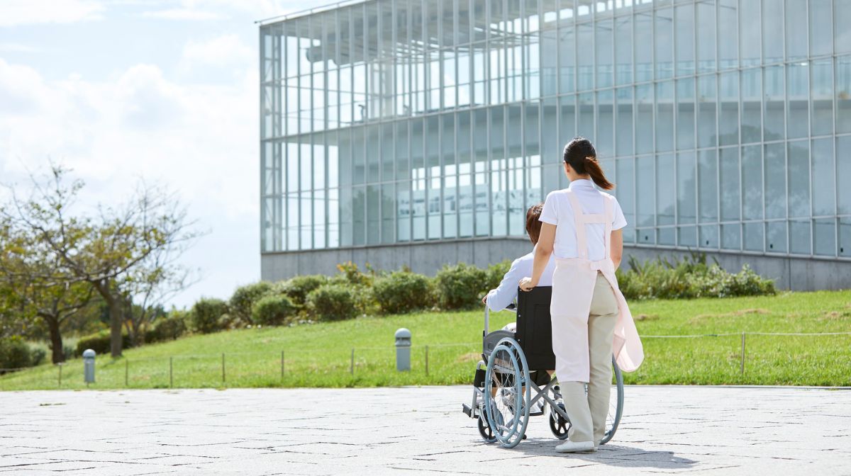 高齢者の座った車いすを押している介護士
