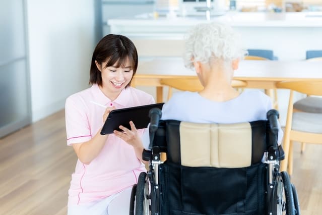 車いすの高齢者と会話をしている介護士