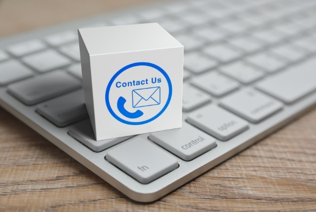 白い立方体に“Contact Us”の文字とメール・電話アイコンが描かれ、パソコンのキーボード上に置かれている画像。問い合わせや連絡ページのイメージ