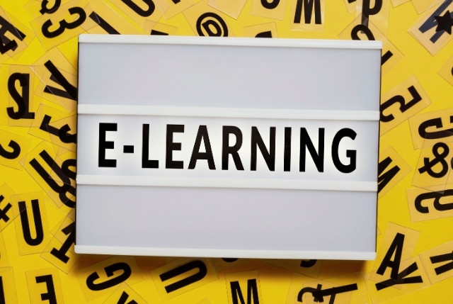 アルファベットが散りばめられた背景に置かれた白いボードに書かれたE-leraningの文字