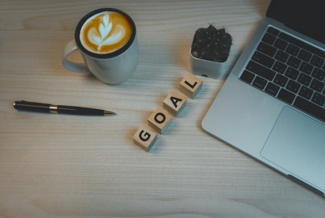 デスクの上に置かれたパソコンとコーヒーカップとGOALと書かれた木のブロック