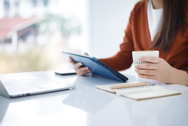 カフェ風のデスクでタブレットとコーヒーを持ちながらオンラインで特定技能の学習をする外国人女性