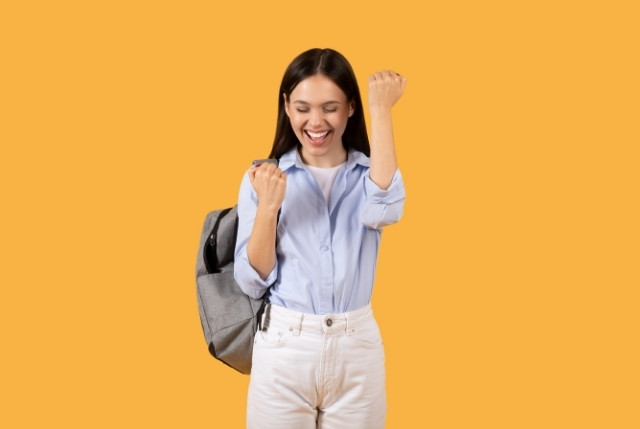 リュックを背負いガッツポーズをする女性学生。明るい表情で試験合格や目標達成の喜びを表現し、JLPT学習の成果や成功イメージを示す