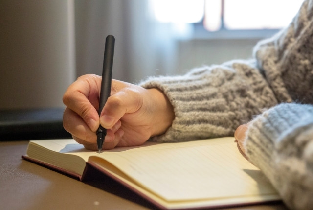 ノートにペンで書き込む手元の写真。日本語の語彙力を高めるための学習やメモを取る様子をイメージ