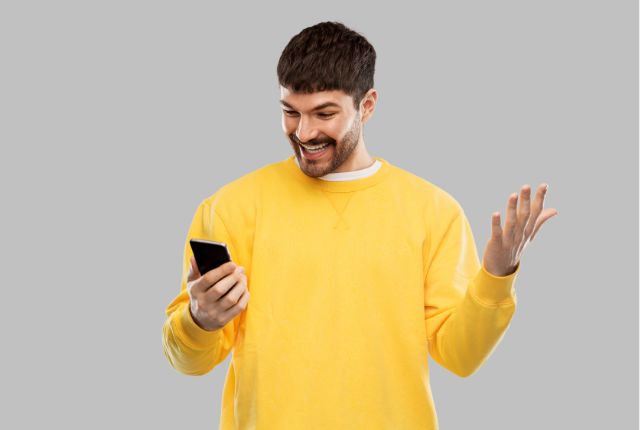 スマートフォンを見て笑顔を見せる男性。外国人社員の日本語学習アプリ利用や漢字練習の楽しさを表すイメージ。