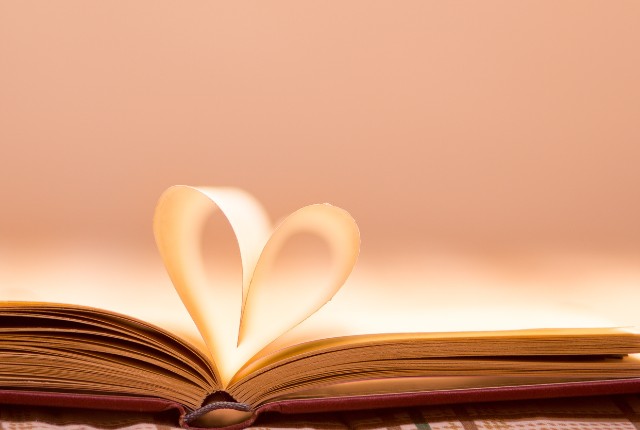 開いた本のページがハート型に折られたロマンチックな構図。学びや読書への愛情、日本語教育への情熱を象徴する写真。