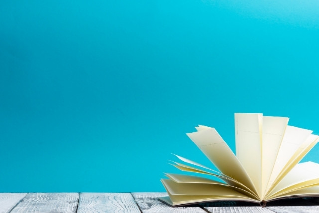 青い背景の前に開かれた本。日本語教育や学習に関する入門書や教材のイメージに適した写真。