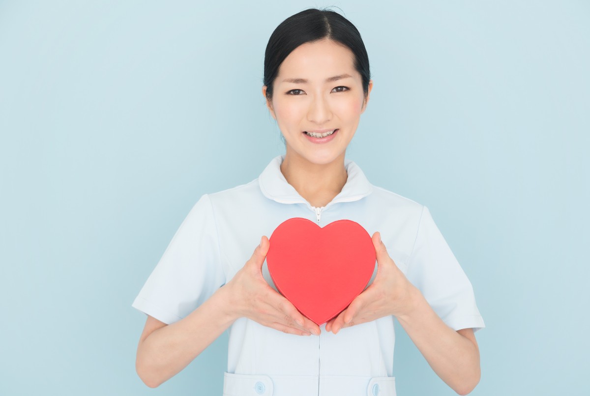 介護職の女性スタッフが赤いハートを胸に持ち、笑顔で思いやりを表現しているイメージ写真。