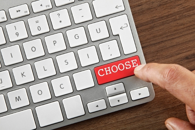 パソコンのキーボードで、赤い「CHOOSE」キーを指で押す瞬間。日本語eラーニング導入の選び方を象徴するイメージ。