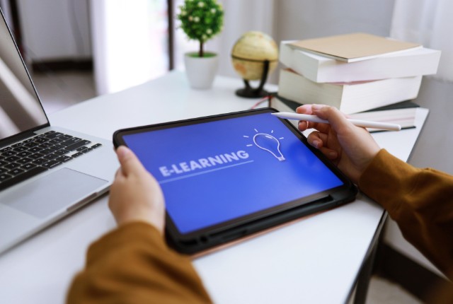 タブレットで「E-LEARNING」と表示された画面を操作する人の手元。企業のオンライン日本語教育やデジタル学習を象徴するシーン。