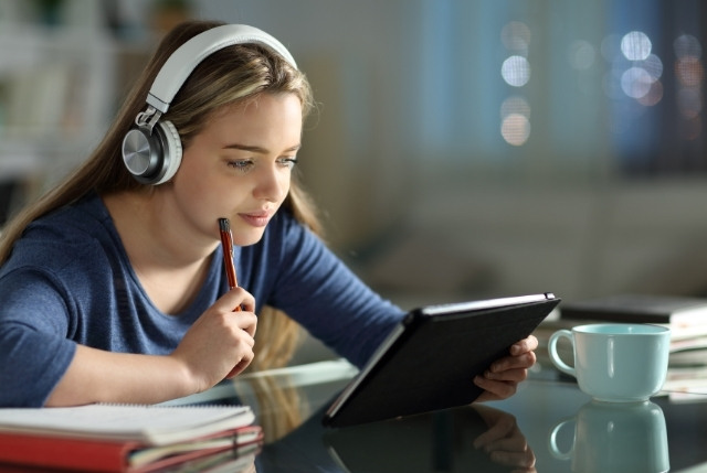 ヘッドホンを着けた女性がタブレットで学習している。日本語eラーニングで自宅学習を行う受講者のイメージ。