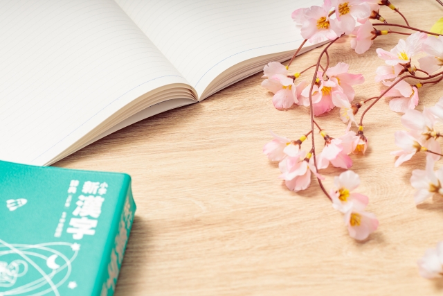 桜の枝と漢字辞典、ノートが並ぶ机。外国人社員の日本語学習モチベーションを表すイメージ写真。