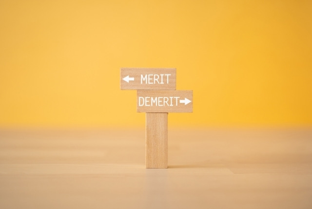 木製の矢印看板に「MERIT」と「DEMERIT」の文字。日本語eラーニング導入のメリット・デメリットを示すイメージ。