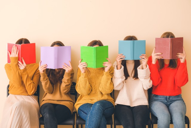 色とりどりの本を手に持ち、顔を隠して読む女性たち。日本語教育の学習や読書を楽しむ姿を表現したイメージ。