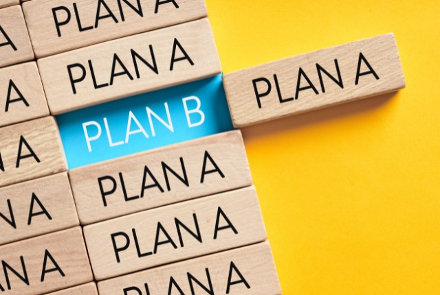 木製ブロックに「PLAN A」と並ぶ中、「PLAN B」だけが青色で際立つ構図。柔軟な戦略変更や代替案の重要性を示すイメージ。