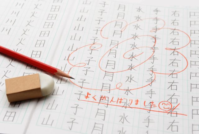 漢字練習帳に赤ペンで添削された学習風景。正しい書き方を確認しながら漢字を繰り返し練習している様子。