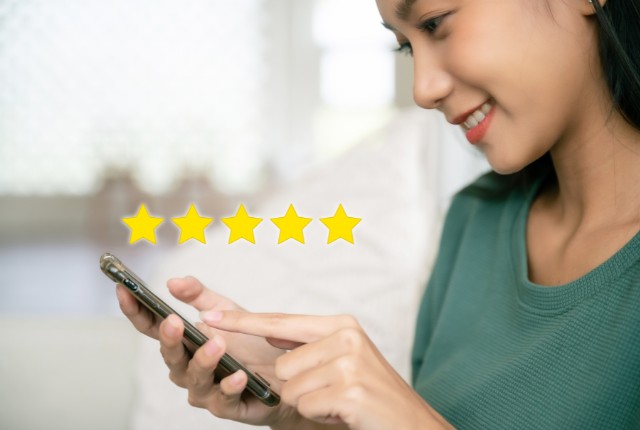 スマートフォンで操作する女性の前に、五つ星評価のアイコンが浮かぶ。外国人スタッフ向け漢字学習アプリの利用イメージ。