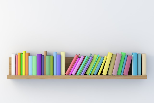 木製の棚に並べられたカラフルな本の背表紙。学びや読書、知識の蓄積をイメージさせる明るい構図。