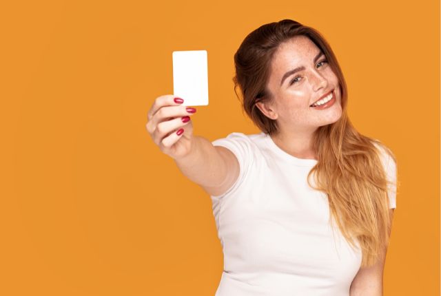 オレンジ色の背景で白いTシャツの女性がカードを手に笑顔を向ける。語学授業やゲーム活動のイメージ。