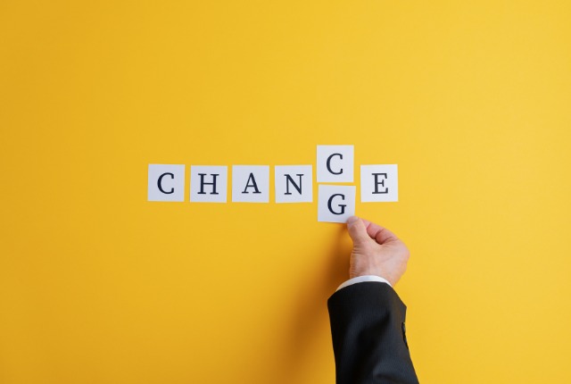 ビジネスマンの手が「CHANGE」の文字を「CHANCE」に変える場面。2号への挑戦や変化を象徴するイメージ。