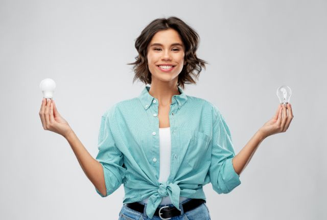 電球を左右に持つ女性が笑顔で立つ写真。選択やアイデアの比較を説明する記事向けのイメージ。