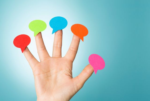 指先に色とりどりの吹き出しが貼られた手の写真。コミュニケーションや多言語表現を示すイメージ。