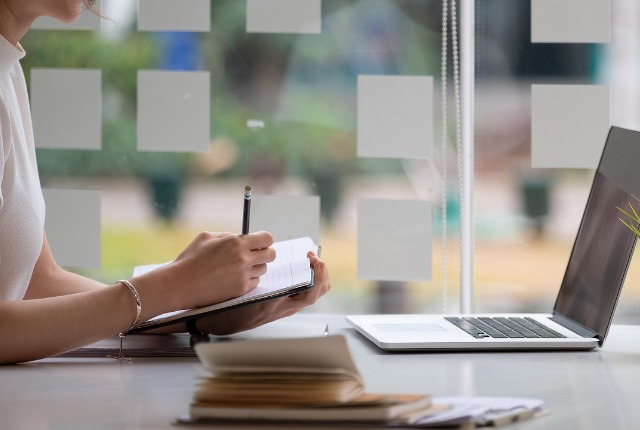 ノートにメモを取りながらオンライン学習する女性。特定技能2号試験対策のオンラインコース受講をイメージ。