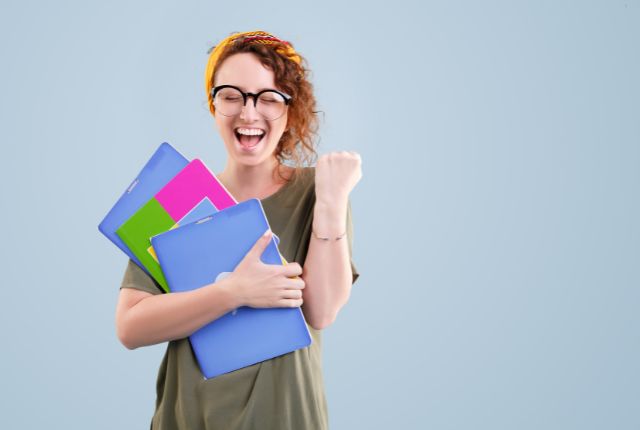 るい表情の女性がカラフルなファイルを抱えてガッツポーズをする。介護福祉士試験の合格や勉強成功をイメージした写真。