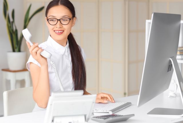 オフィスで電話対応をしながらパソコンを操作する女性スタッフのイメージ