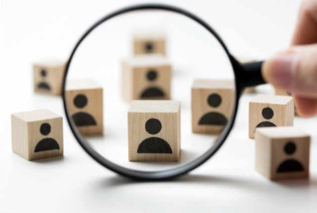 人材を象徴する木製ブロックを虫眼鏡で拡大して選別する様子。採用活動や人材選びのイメージ。