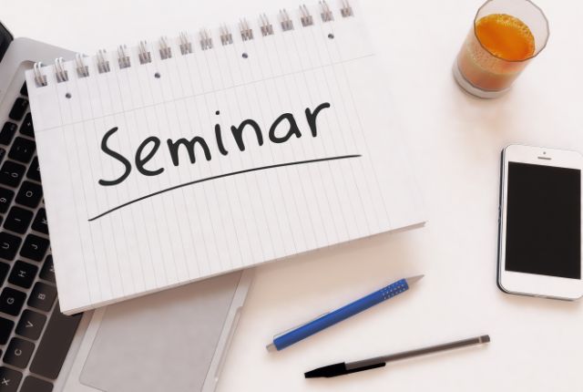 ノートに「Seminar」と書かれた文字とノートパソコン、スマートフォン、ペンが並ぶ机上のイメージ。オンラインセミナーや学習準備の象徴。