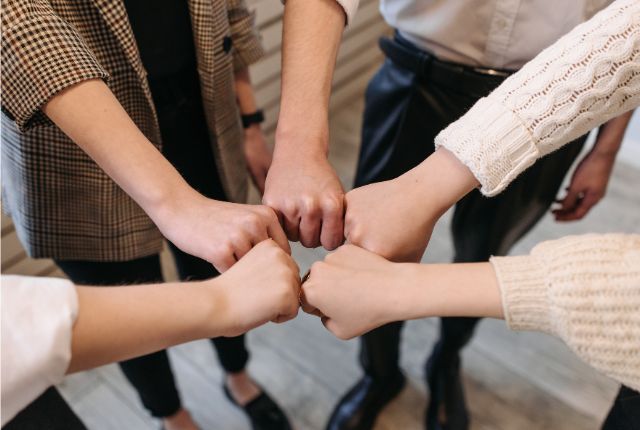 複数の人が円を作り、拳を合わせて団結を示す場面。チームワークや職場での協力体制を象徴する画像。
