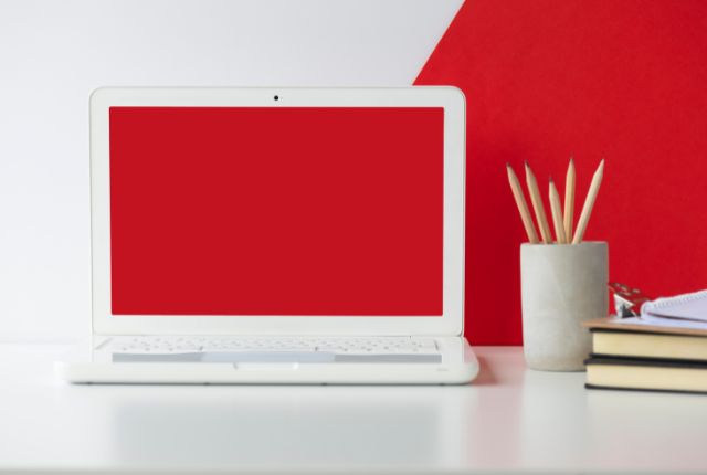 赤い画面のノートパソコンが置かれたデスク環境｜学習や作業スペースのイメージ・オンライン利用シーン