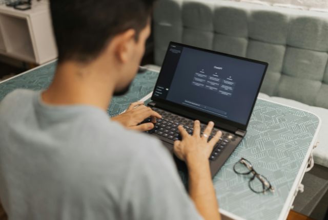 ノートパソコンで作業する男性の背面姿。画面にはAIツールの操作画面が表示され、デジタル学習の様子を示す写真