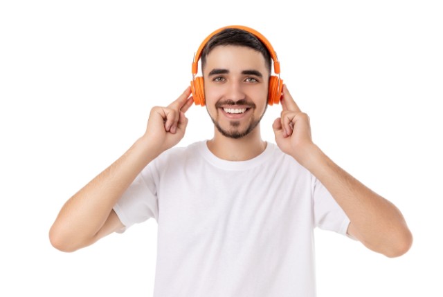オレンジのヘッドホンで音声を聴きながら笑顔の男性。語学リスニングや音声学習を楽しんでいる場面のイメージ。