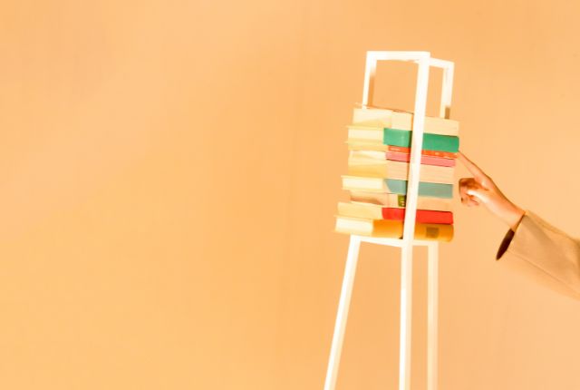 積み重ねた本を手に取る様子、学習教材や知識の積み上げを表すビジュアル