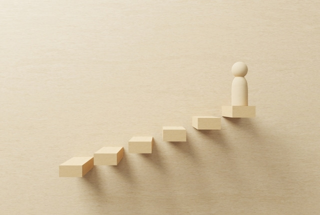 段階的な成長やキャリア形成を表す、階段状のブロックを上る人物オブジェのイメージ