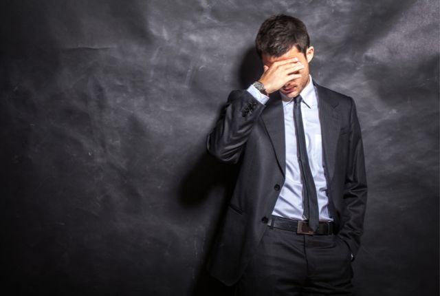 頭を抱えて悩むスーツ姿のビジネスマン。日本語教育の業務負担や課題に直面する様子