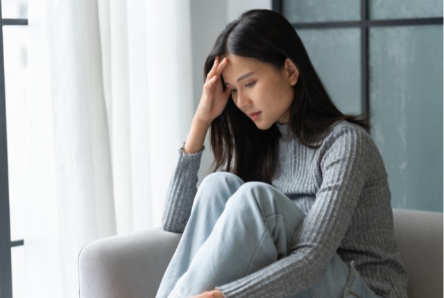 ソファに座り頭を抱えて悩む女性の写真。ストレスや不安を抱える様子を表し、メンタルケアや悩み相談のイメージに最適。
