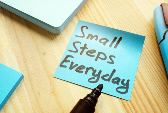 「Small Steps Everyday」と書かれた付箋とペンが置かれた、学習や目標達成をイメージしたデスクの写真