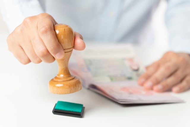 外国人労働者の在留資格を確認するため、書類にスタンプを押す様子。採用時に必要な資格審査のイメージ