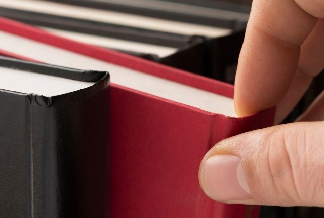 棚から赤い本を指で取り出そうとしている手元のクローズアップ