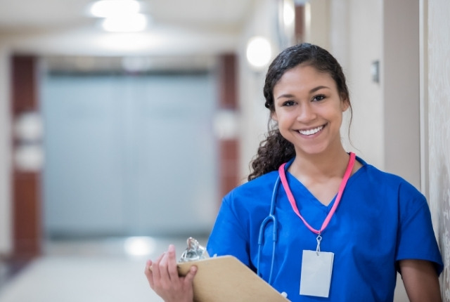 外国人介護士と支える介護現場 介護施設の廊下で、クリップボードを持ち笑顔で立つ介護士の様子