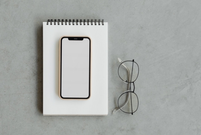 ノートの上に置かれたスマホと眼鏡の写真。学習や調べ物をする場面のイメージ。