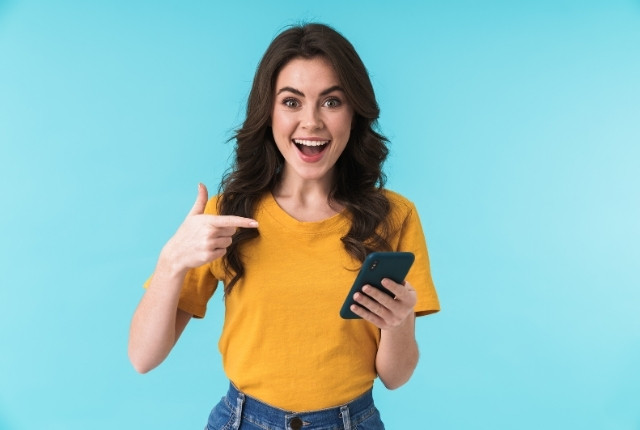 スマホを手にして驚いた表情を見せる女性の写真。アプリを示しているイメージ。