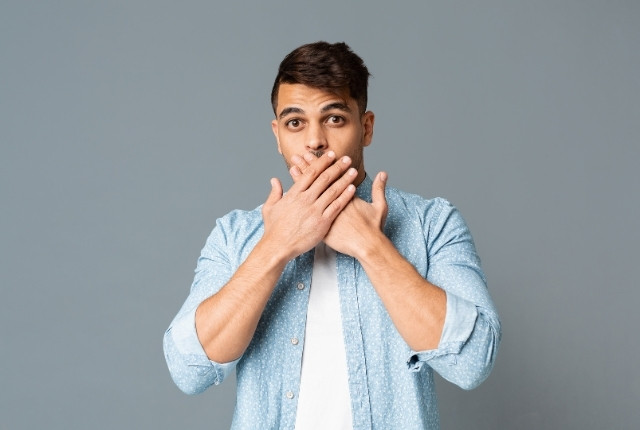 両手で口元を覆い驚いた表情を見せる若い男性のポートレート