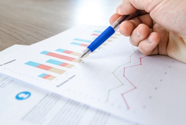 介護福祉士試験の合格率データ 棒グラフと折れ線グラフが印刷された資料を、青いペンで指し示している手元の写真