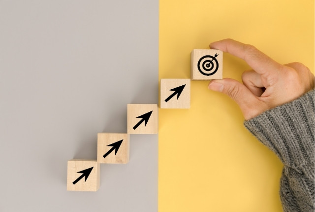 矢印が描かれた木製ブロックを階段状に並べ、目標マークのブロックを手に取る様子