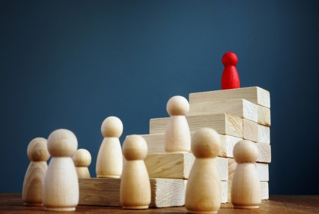 木製の人形が段差状に並び、赤い人形が一段高い位置に置かれている構図の写真