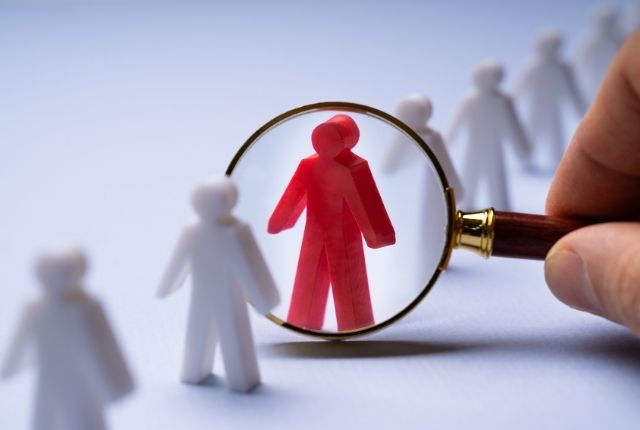 虫眼鏡で赤い人物模型を拡大し人材選定を表現したイメージ写真